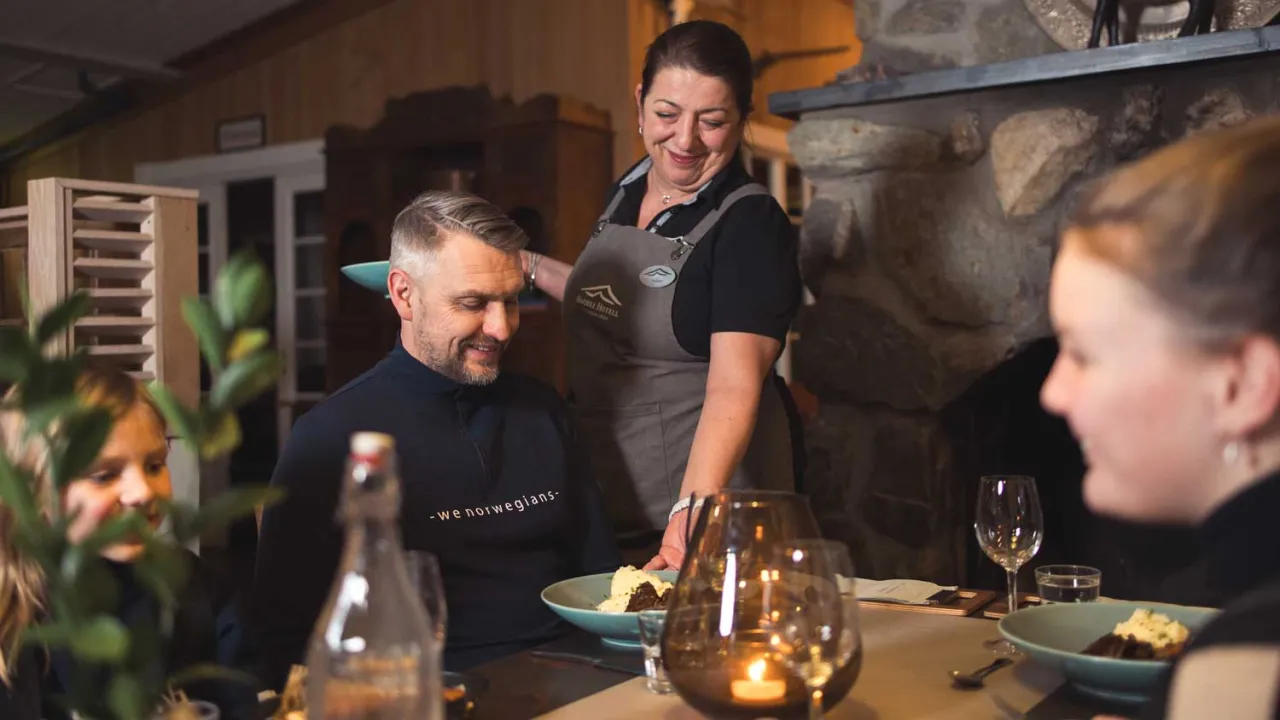 En servitør serverer mat til en mann som sitter ved et bord sammen med to jenter